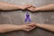 Man and woman holding hands and purple awareness ribbon on marble background