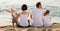 Man and woman with kids sitting with back to camera on beach