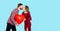 Man and woman kiss on a blue background and hold in their hands a large inflatable red ball in the shape of a heart. Concept of