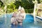 Man and woman, loving couple, in pool in a garden with tropical trees hold glasses with wine in hand