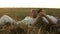 Man and a woman are lying on haystack holding hands in a meadow at sunset in Slowmo