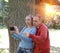 Man and woman near an oak in summer day show to the side and photograph on phone