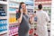 Man and woman pharmacist and pregnant client talking on smartphone holding medication bottle at pharmacy