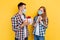 Man and a woman in plaid shirts and medical protective masks, a happy man gives a gift to his girlfriend, on an isolated yellow