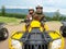 A man and woman of retirement age in camouflage suits and helmets ride a yellow ATV in the mountains. Sports, recreation