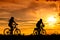 A man and a woman ride bicycles on the road with beautiful colorful sunset sky