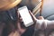 Man and woman`s hands holding and looking at white mobile phone with blank desktop screen together