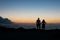 A man and a woman in silhouette looking towards the horizon at the setting sun over the Mediterranean