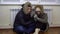 A man and a woman sit on the floor in their jackets by the radiator and warm themselves. A young married couple have not