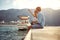 Man and woman sitting on the lake pier dangling legs and drinking beer