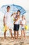 man and woman with two kids standing together under beach umbrella on beach