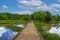 A man and a woman walking down a long winding wooded bridge in the forest surrounded by lush green trees and plants with blue sky