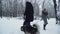 A man and a woman walking with huskies holding them on a leash pass by each other in a winter snow-covered park. Dogs on