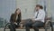 Man and woman wearing formal suit sitting in front of the corporate building on the bench and laughing and talking in coffee break