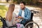 A man and a woman in wheelchairs met in the park. They exchange gifts and smile at each other.