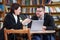 Man and woman working with laptop sitting in modern stylish room with bookshelves on background in library or bookstore