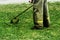 Man in work clothes mows green grass with a trimmer
