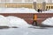 Man worker of communal service in orange special clothes cleans street in center of city from snow after heavy snowfall in March