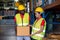 A Man worker holding a box or parcel and listen to a woman in the large warehouse distribution center. Both engineers people wear
