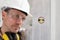 Man worker looks at the spirit level checks the wall with hard hat, glasses and ear protection headphones, close up