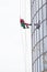 A man worker in red worksuit cleaning the exterior windows of a skyscraper - industrial alpinism at overcast weather -