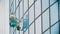 A man worker in yellow work clothes hanging on ropes and wipes the exterior windows of a business skyscraper -