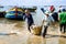 Man workers carrying deep bamboo basket loaded with fish at Long Hai fish market, Ba Ria Vung Tau province, Vietnam.