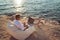 Man working on his laptop lying on deck chair on the beach during sunset