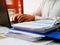 A man works at a computer in the office. Pile of financial performance papers