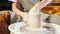 Man works his hands with clay. Process of creating product from clay on potter`s wheel. Side view of artisan making pot