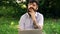 Man works with a laptop in the park. A student emotionally works with a notebook while sitting on a grass in a park