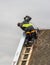 A man works on the roof repair, installs sheet metal on top of the gable wall