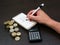 Man writing down on a notebook while counting colombian currency coins of different nominations over a table with a calculator