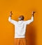 Man in years in white hoodie, pants and sunglasses, bracelets. Raised hands up, laughing, posing on orange background. Close up