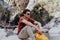 Man with yellow backpack sits on a riverside rock in the canyon with mountain cliffs in the background. Adult man taking