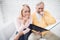 A man in a yellow cardigan and a woman in a pink sweater are sitting and reading documents in a black folder.