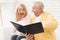 A man in a yellow cardigan and a woman in a pink sweater are sitting and reading documents in a black folder.