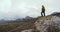 A man in a yellow jacket stands on a stone against a background of snow-covered mountain peaks in a fog