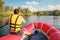 A man in a yellow life jacket with an oar floats in an inflatable boat on the river.