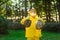 A man in a yellow protective suit and mask holds bags of garbage and shows class with his hands