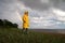 Man in yellow raincoat with hood walk on the beach in rainy weather, looks at dramatic cloudy sky and sea, rainbow on background