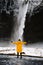 A man in a yellow raincoat stands facing a waterfall back view. The most beautiful and powerful waterfalls in Iceland. Nature and