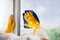 Man in yellow rubber gloves cleaning window glasse with cleaner spray detergent and squeegee Housework and housekeeping, home