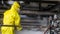 A man in a yellow waterproof suit and face shield is cleaning a heat exchanger with a high pressure device