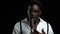 Man young african american singing into a microphone in a recording studio. Black background. Slow motion. Close up