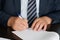 A manager, civil servant or lawyer in a dark suit signs a document. Conducting correspondence. Close-up. Shallow depth of field