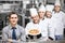 Manager standing in front of chefs holding pizza in kitchen