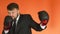 Manager in suit and gloves is boxing and throws punches at the camera in slowmo on orange background. Cheerful plump