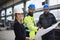 Manager supervisor, engineer and industrial worker in uniform discussing blueprints in large metal factory hall.