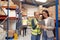 Manager Using Digital Tablet With Female Intern Inside Busy Warehouse Facility